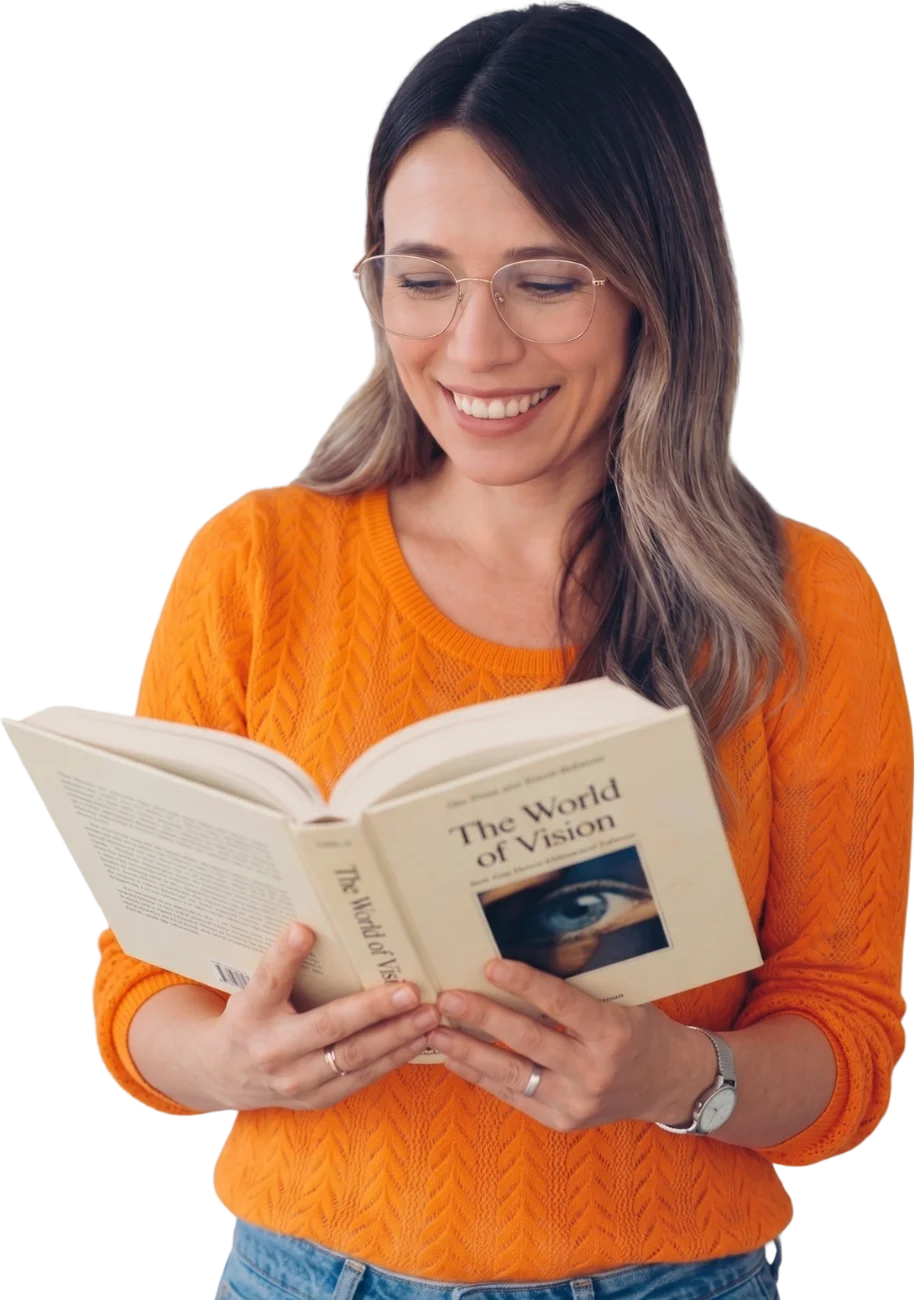 Woman in glasses smiling as she reads The World of Vision